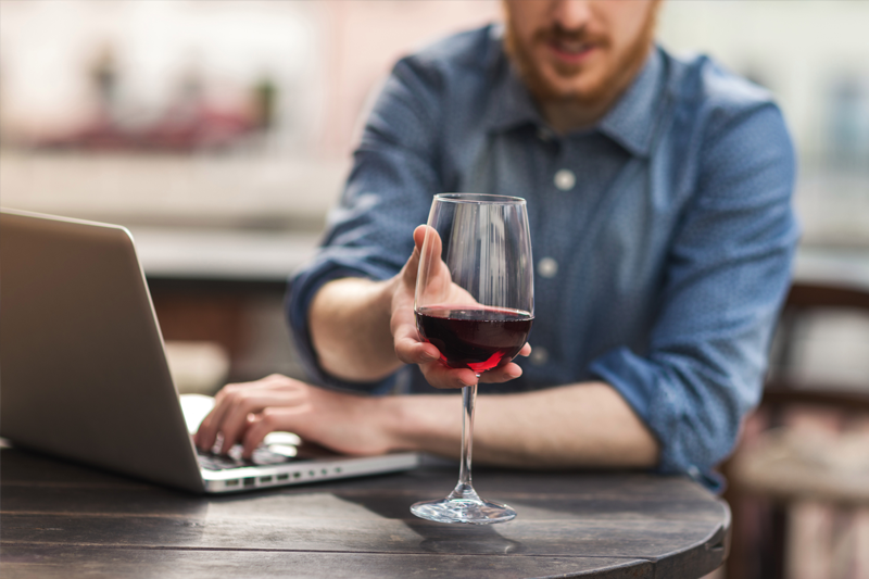 Man at computer reaching for glass of wine.